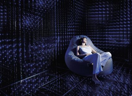 Una donna si rilassa su una poltrona morbida in una sala buia con pareti illuminate da punti di luce blu.