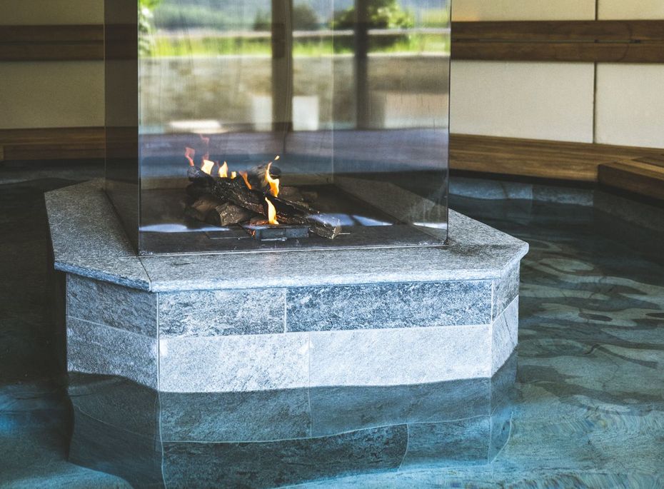 Ein moderner Kamin steht mittig in einem ruhigen Wellnessbereich mit Wasserbecken.