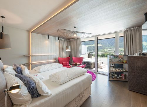 Helles Schlafzimmer einer Luxury Suite mit Doppelbett, Sitzecke und bodentiefen Fenstern zum Balkon mit Bergblick.