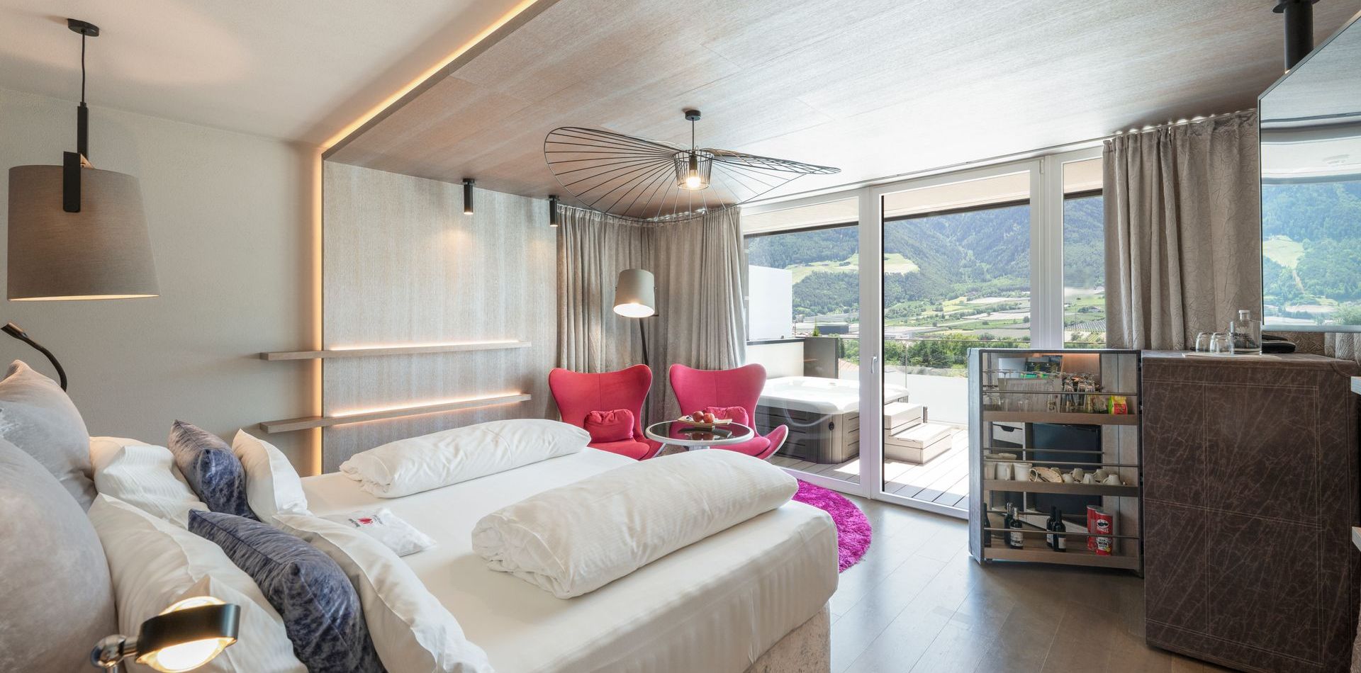 Helles Schlafzimmer einer Luxury Suite mit Doppelbett, Sitzecke und bodentiefen Fenstern zum Balkon mit Bergblick.