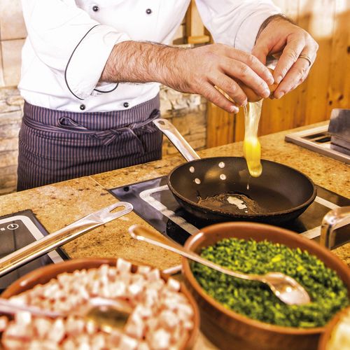 Ein Koch lässt frische Pasta in eine Pfanne in der Gourmetküche gleiten, daneben stehen Schalen mit gehackten Zutaten.