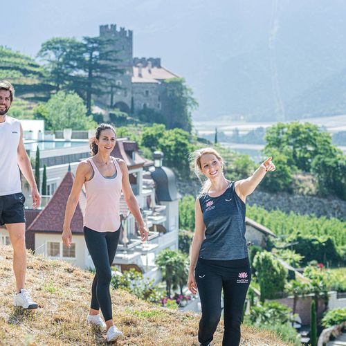 Drei Personen wandern auf einem sonnigen Hang mit Blick über die Landschaft bei Naturns.