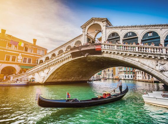 Eine Gondel fährt unter der Rialtobrücke in Venedig über das grüne Wasser des Kanals.