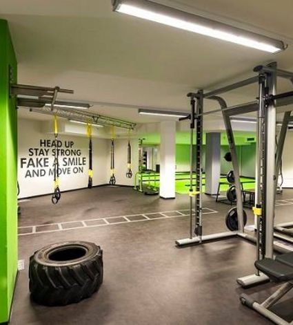 Ein heller Fitnessraum mit Trainingsgeräten, Hantelablage, Battle Rope und großem Reifen für funktionelles Training.