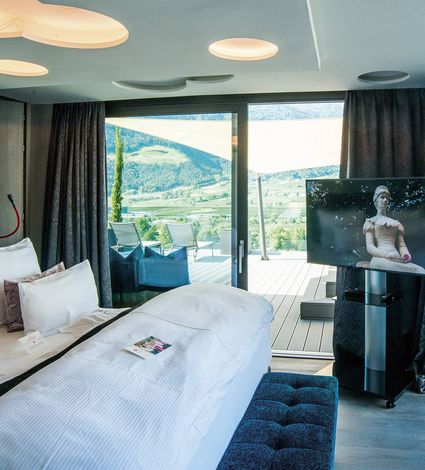 Ein modernes Hotelzimmer mit Doppelbett, Fernseher und Balkon mit Blick auf die Berge.