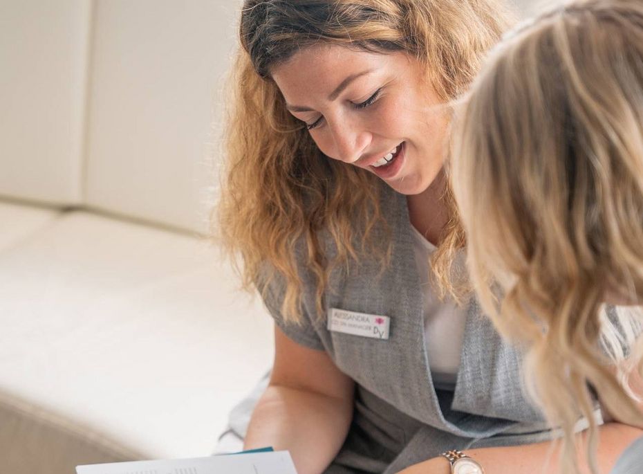 Wellnessberatung im Preidlhof in Naturns Eine Mitarbeiterin erklärt einer Frau im Lounge-Bereich ein Informationsheft.