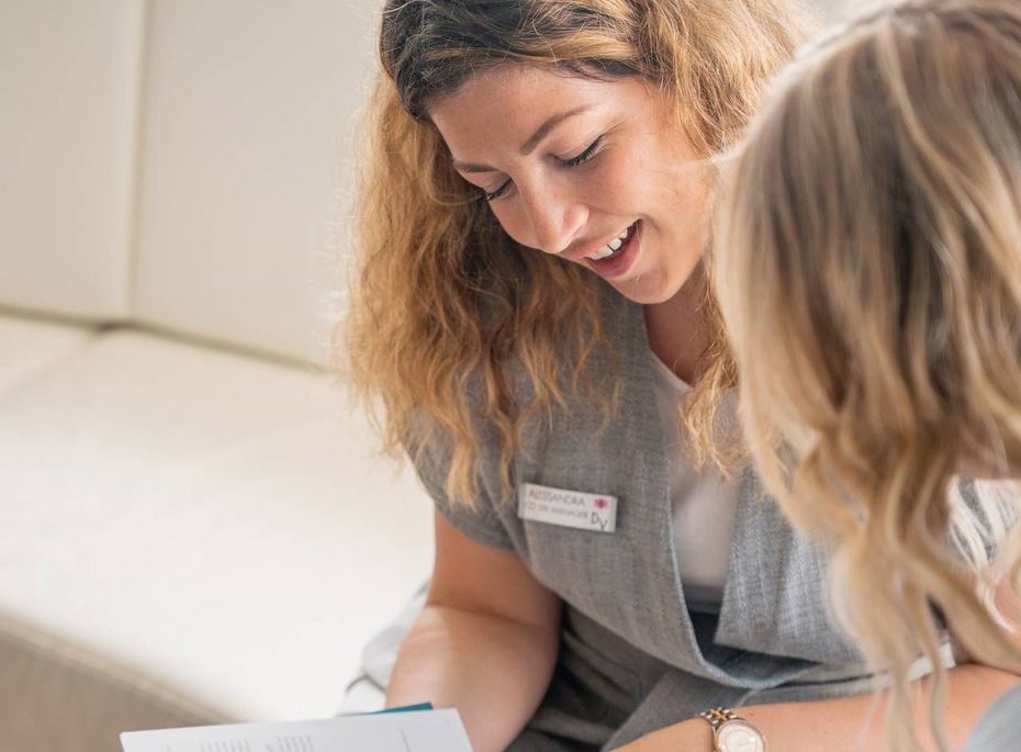 Wellnessberatung im Preidlhof in Naturns Eine Mitarbeiterin erklärt einer Frau im Lounge-Bereich ein Informationsheft.