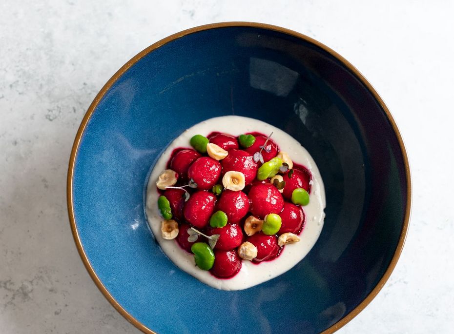 Dessert mit Beeren im Preidlhof Eine blaue Schale mit cremigem Dessert, belegt mit Erdbeeren, Himbeeren und kleinen grünen Früchten, steht auf hellem Untergrund.
