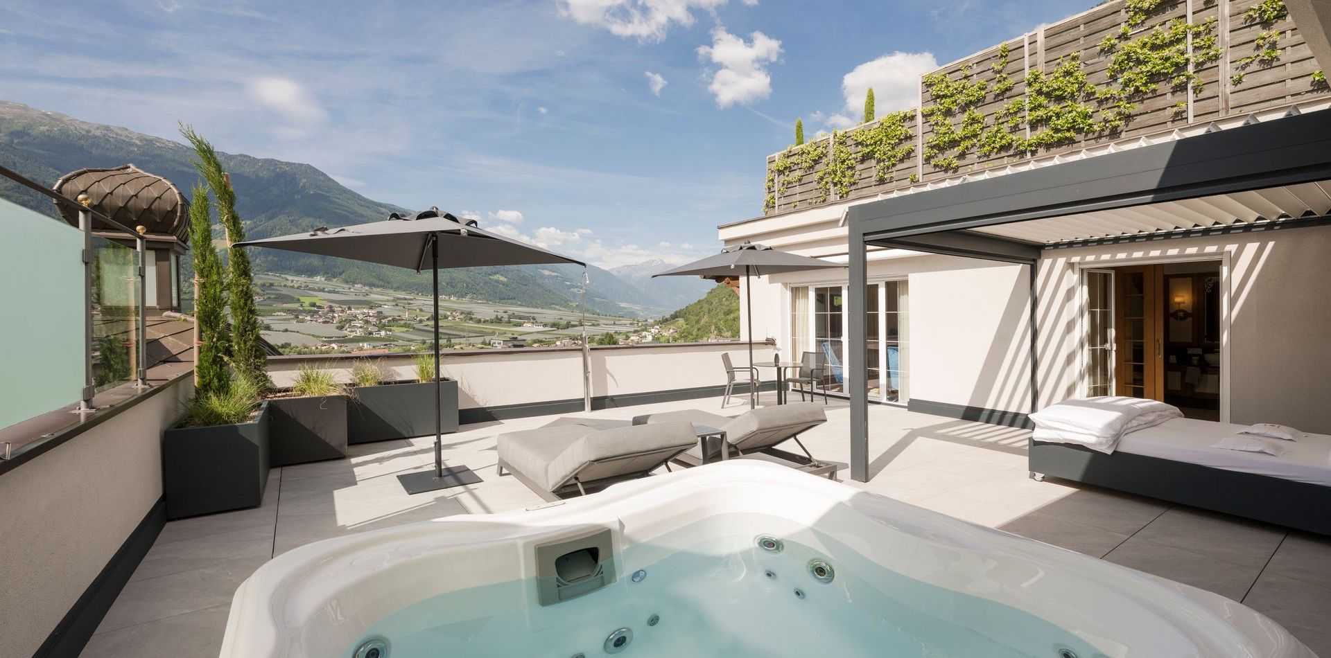 Eine Dachterrasse einer Luxussuite mit Whirlpool, Liegen, Sonnenschirm und Blick auf die Berge.