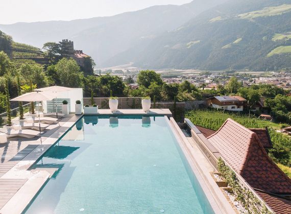 An infinity pool overlooks the valley and mountains beside a terrace with umbrellas and loungers.