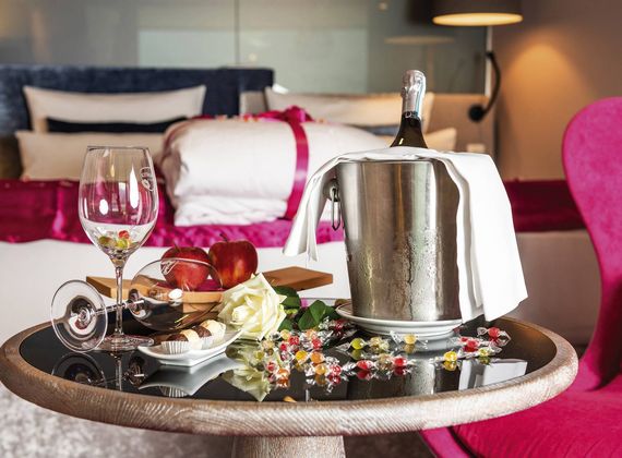 Eine Champagnerflasche im Eisbehälter steht auf einem Tablett mit Glas und Obst auf dem Bett im Zimmer.