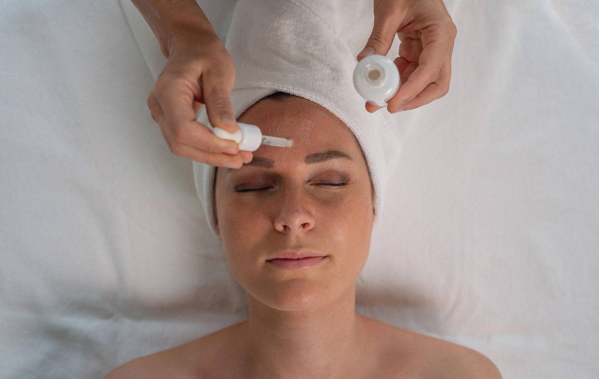Eine Frau erhält eine Kosmetikbehandlung im Gesicht, während eine Pflegerin Produkte aufträgt.