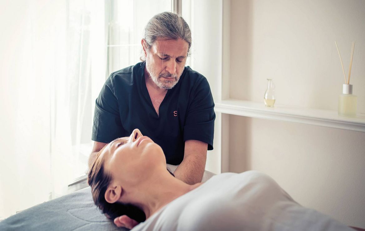 A therapist performs a massage treatment while a woman lies on a spa bed.