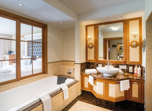 Luxury suite bathroom at Preidlhof A luxury suite bathroom with a bathtub, marble vanity, large mirror, and sliding doors to the bedroom.