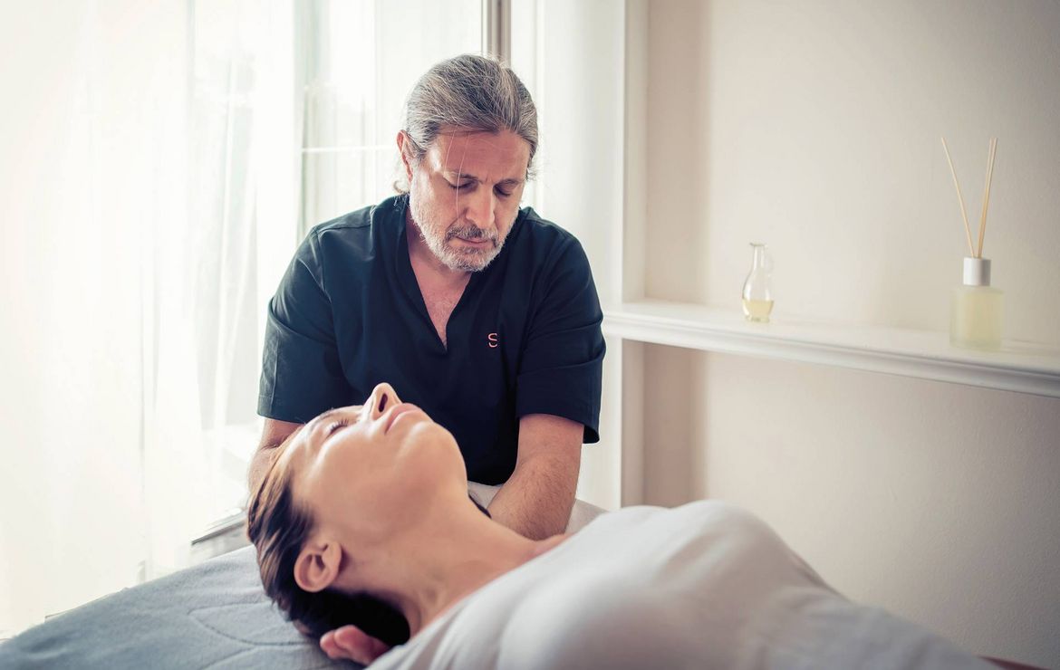 Ein Therapeut behandelt eine liegende Frau bei einer Massage in einem hellen Behandlungsraum.