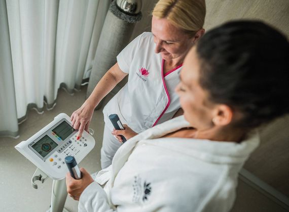 Eine Mitarbeiterin erklärt einer Frau die Bedienung eines Behandlungsgeräts im Medical Spa.