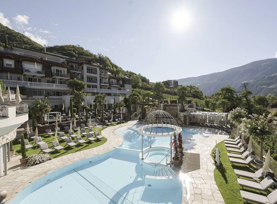 An outdoor infinity pool curves through the pool landscape at Preidlhof, surrounded by loungers, terraces and mountain views.