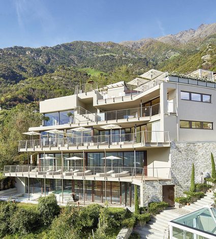 Das moderne Spa Hotel mit mehreren Terrassen liegt vor einer Bergkulisse.