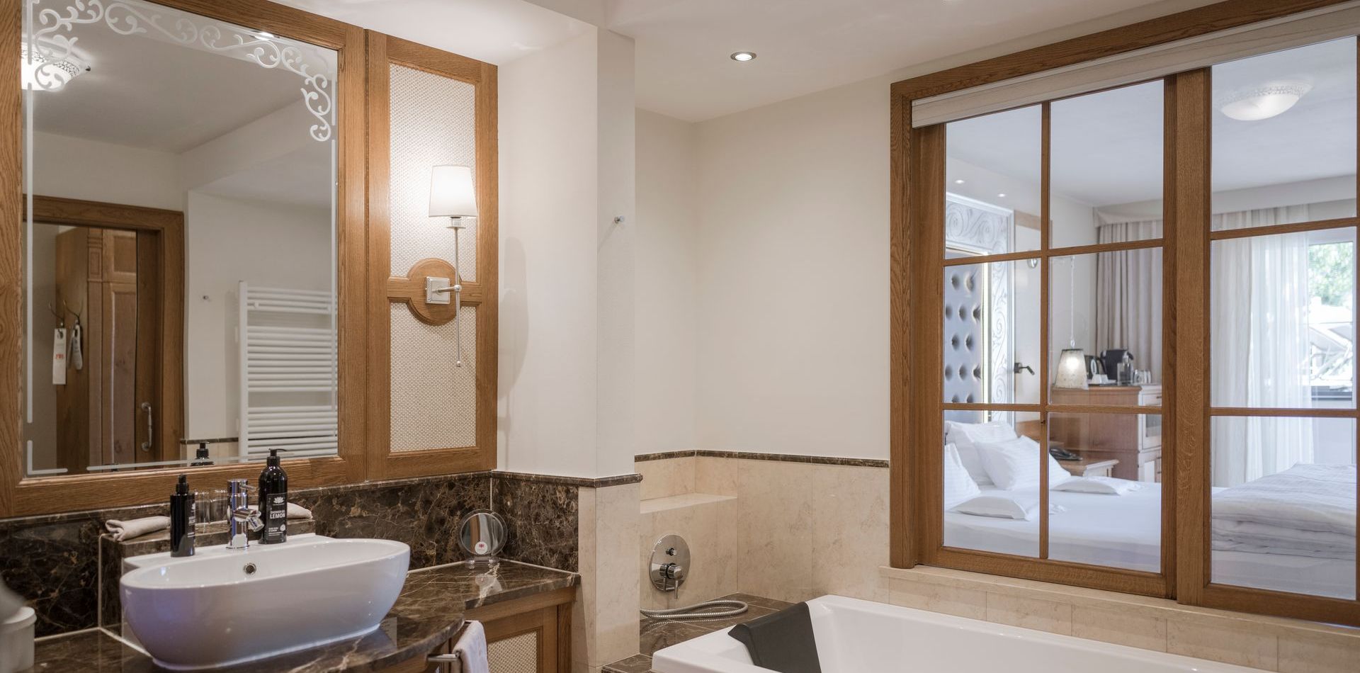 Ein helles Bad mit Doppelwaschbecken, Spiegel, Badewanne und Blick ins Schlafzimmer der Luxury Suite Lantana.