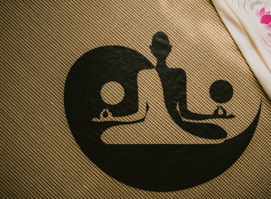 Eine Spa-Matte mit schwarzem Meditationssymbol liegt auf einer strukturierten Oberfläche.