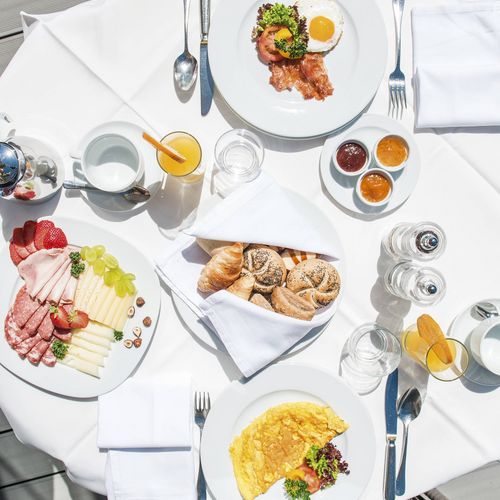 Ein gedeckter Frühstückstisch mit Eierspeise, Gebäck, Aufschnitt, Käse, Marmeladen und Getränken auf der Terrasse.