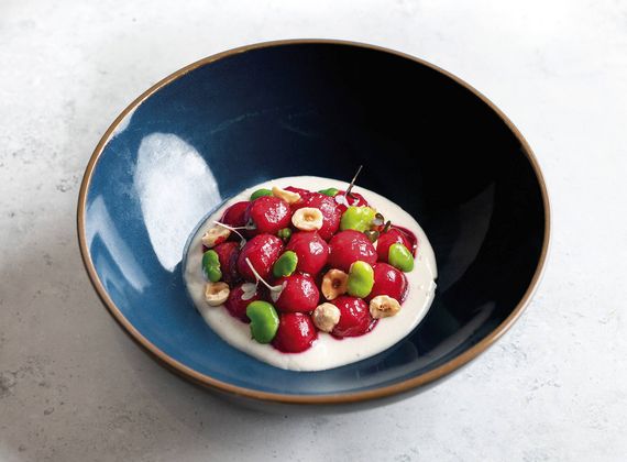 Una ciotola scura contiene un dessert gourmet con frutti rossi, guarnizioni verdi e crema.