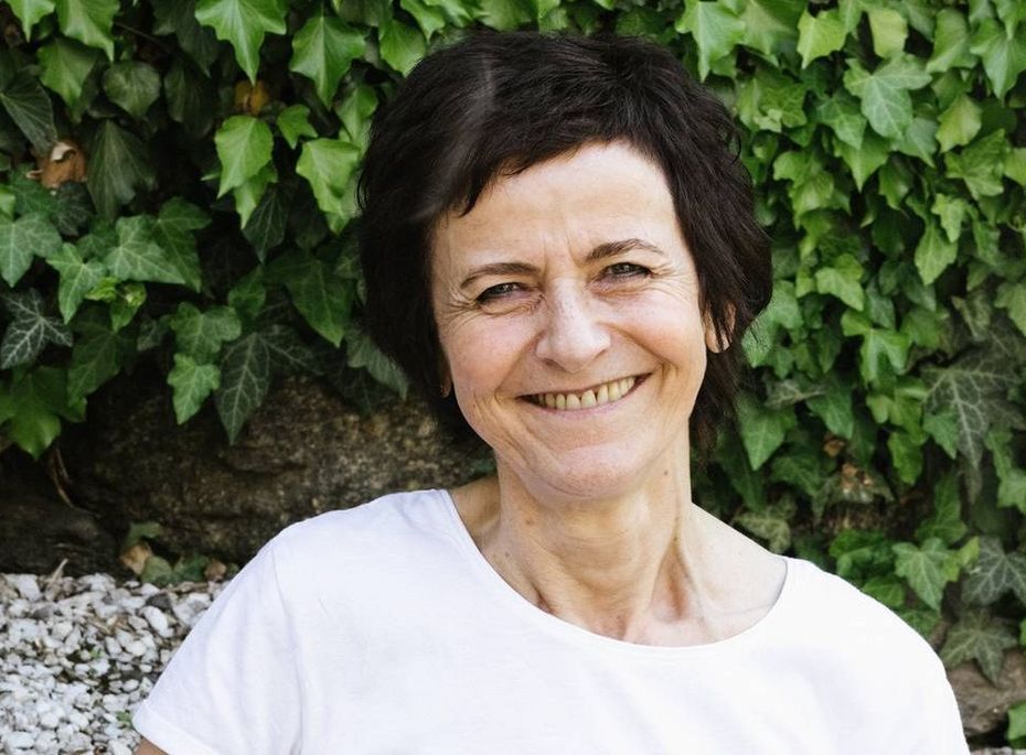 Mitarbeiterin im Preidlhof vor Efeuwand Eine lächelnde Mitarbeiterin steht in weißer Kleidung vor einer grünen Efeuwand und Steinen.