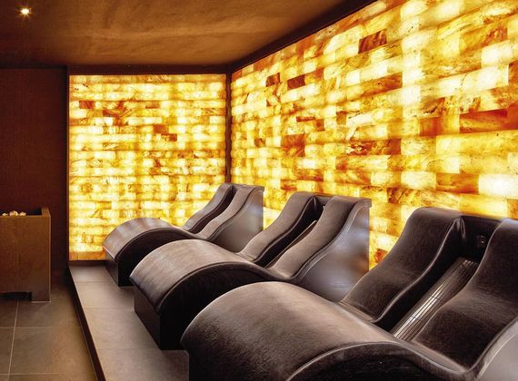 Four reclining loungers sit in a warm relaxation lounge with glowing backlit stone walls.