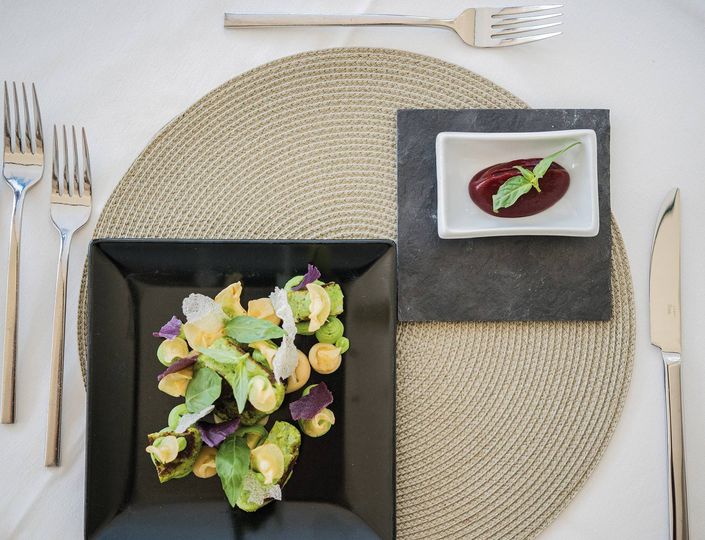 A gourmet salad in a black bowl sits beside beetroot sauce on a slate plate at a neatly set table.