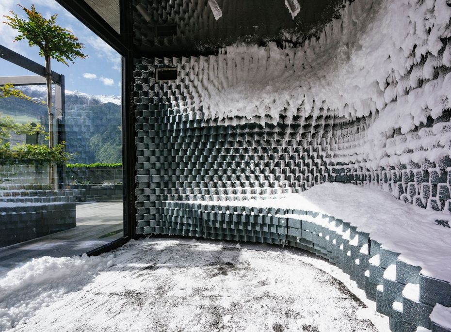 Schneeraum im Spa des Preidlhof in Naturns Ein Schneeraum mit weißer Frostwand und Liegebank neben großer Glasfront mit Bergblick.