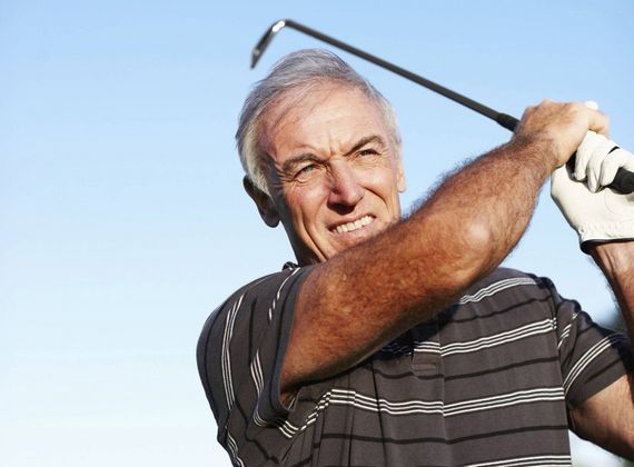 Ein älterer Mann schwingt auf dem Golfplatz einen Golfschläger vor blauem Himmel.