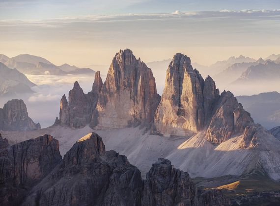 Cime dolomitiche frastagliate emergono sopra un paesaggio alpino velato dalla luce serale.