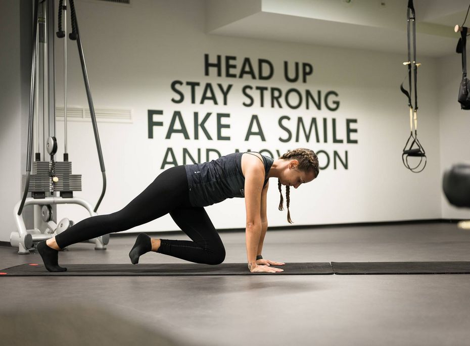 Fitnessraum im Wellnesshotel in Naturns Eine Frau trainiert auf einer Matte im Fitnessraum, während im Hintergrund motivierende Wandzitate zu sehen sind.