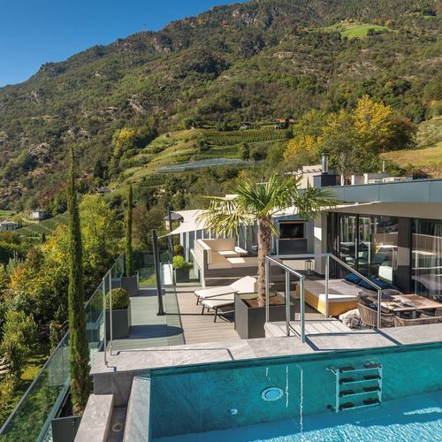 Ein Infinity-Pool auf der Terrasse mit Blick auf die Berge und die modernen Zimmer des Wellnesshotels.