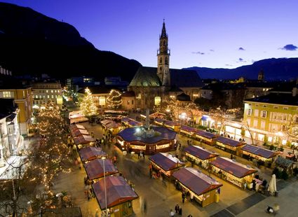 Der Weihnachtsmarkt ist abends mit beleuchteten Ständen und einer Kirche im Hintergrund zu sehen.