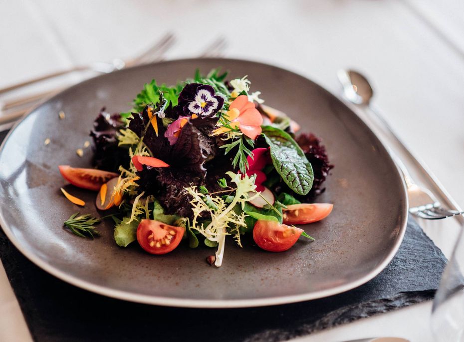 Gourmetsalat im Preidlhof in Naturns Ein kunstvoll angerichteter Gourmetsalat mit Blüten, Kräutern und Tomaten auf einem dunklen Teller.