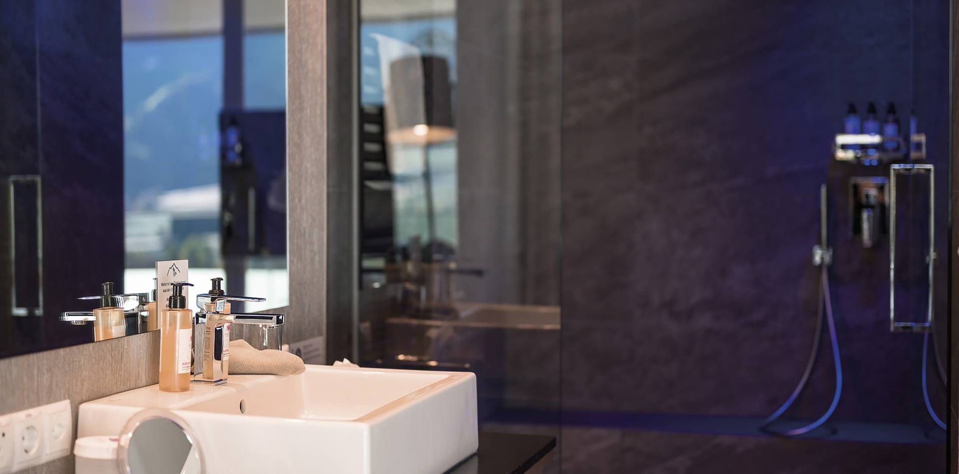 A sleek bathroom with a white vessel sink, dark surfaces and a glass shower in the Single Suite Blue.