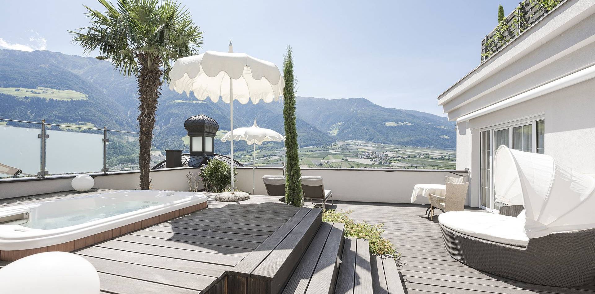 A rooftop terrace with a whirlpool, lounge seating and mountain views beside the suite.