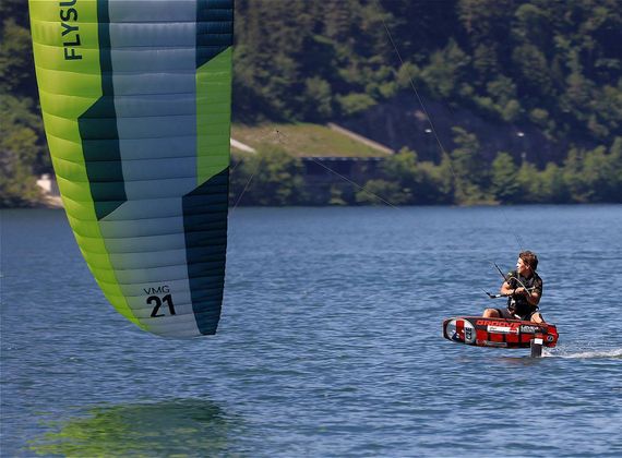 Ein Kitesurfer fährt auf dem Reschensee, während das grün-blaue Segel links im Bild zu sehen ist.
