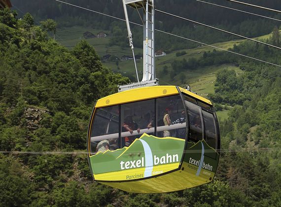 Eine gelbe Gondel der Texelbahn fährt vor grünen Hängen durch die Berglandschaft.