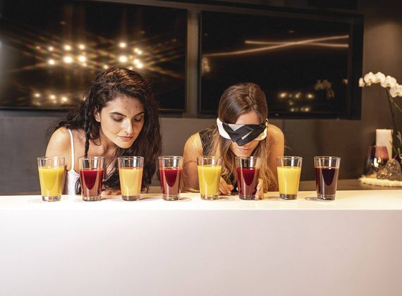 Two women sample assorted wellness juices behind a counter in a softly lit lounge.