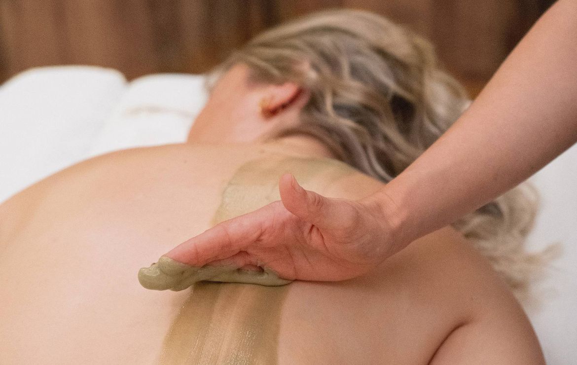 Una terapista applica un trattamento corpo lungo la schiena di una ospite durante un massaggio spa.