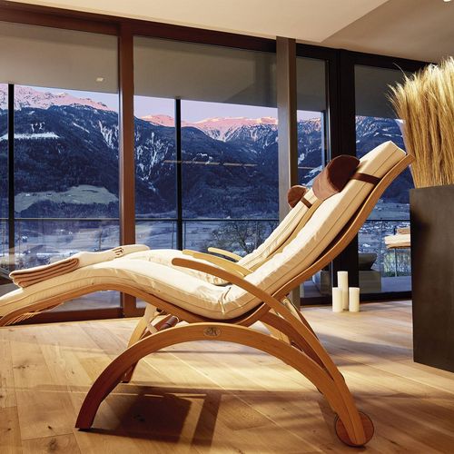 Eine Ruheliege steht vor großen Fenstern mit Blick auf verschneite Berge und den Innenraum des Spa.