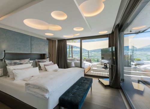Die Penthouse Suite zeigt ein großes Bett, dunkle Vorhänge und eine Glasfront mit Blick auf die Berge.