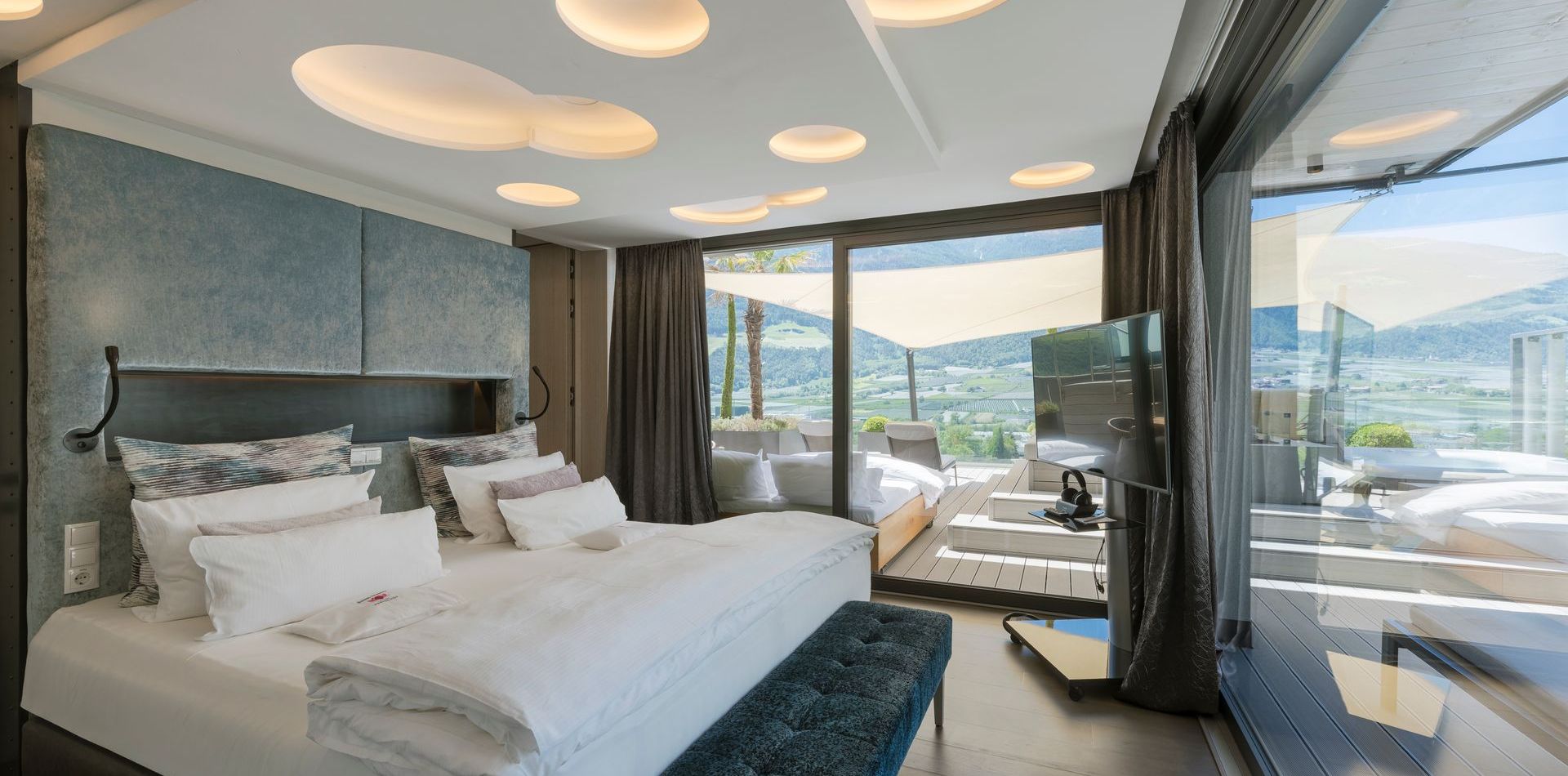 Die Penthouse Suite zeigt ein großes Bett, dunkle Vorhänge und eine Glasfront mit Blick auf die Berge.