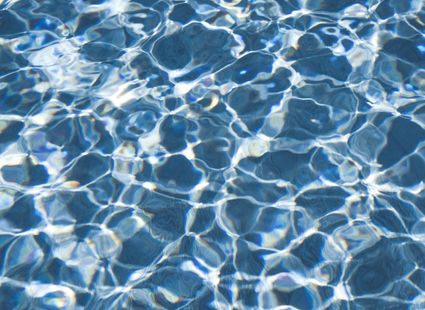 Nahaufnahme von blauem Poolwasser mit hellen Lichtreflexen und bewegten Wellen.
