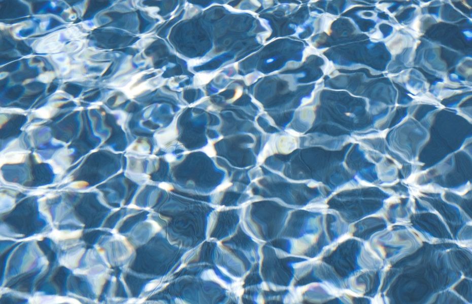 Nahaufnahme von blauem Poolwasser mit hellen Lichtreflexen und bewegten Wellen.