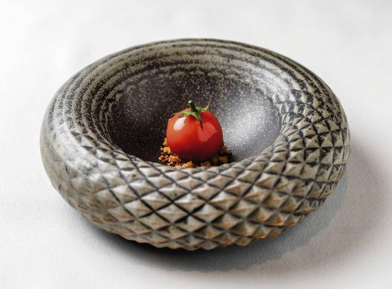 A small tomato garnish sits in a textured ceramic bowl on a white tablecloth.
