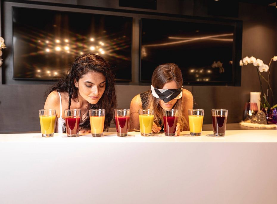 Saftauswahl an der Bar im Preidlhof Zwei Frauen wählen an der Bar zwischen mehreren farbigen Saftgläsern aus.