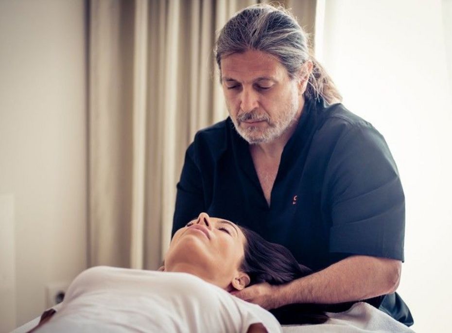 Ein Therapeut behandelt eine liegende Frau bei einer Massage im hellen Behandlungsraum.